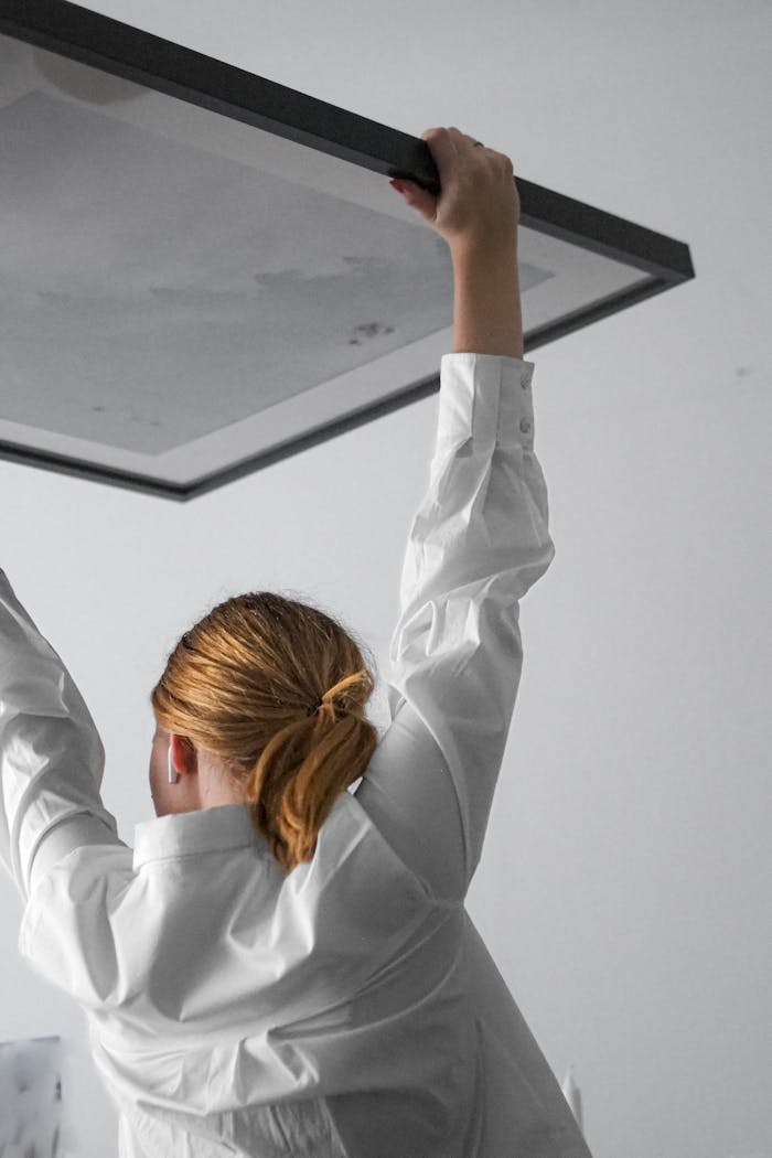 Home Woman in white shirt adjusting a ceiling light fixture with focused attention.