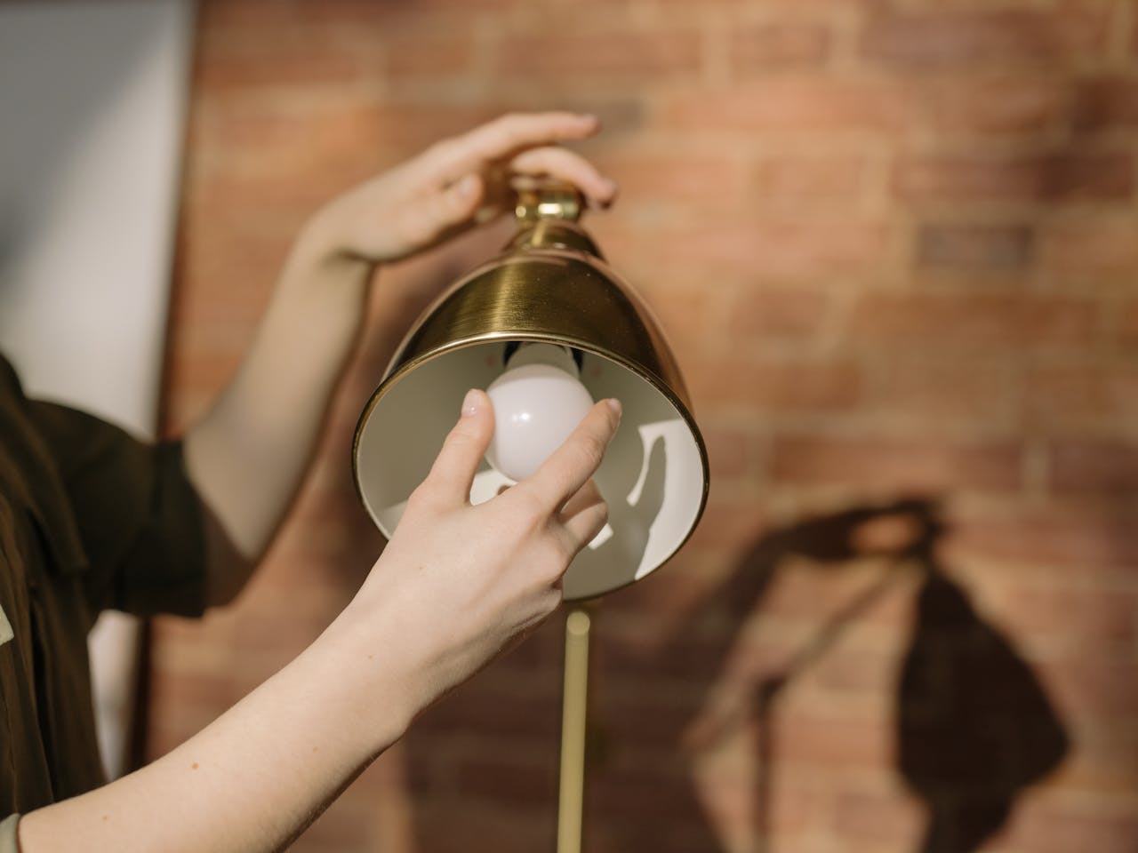 Services Hands changing a light bulb in a lamp with a brick wall background.